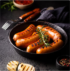 Grilled sausages in a cast iron skillet with rosemary on a dark surface.